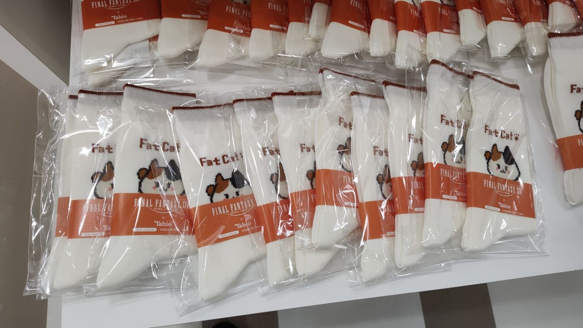 Une pile de chaussettes Fat Cat de Tobio se trouve sur une table d'exposition lors de l'événement A Decade's End Final Fantasy XIV