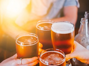 Verres à bière portés en toast.  Mains en gros plan avec des lunettes.  Intérieur du bar flou à l'arrière-plan.