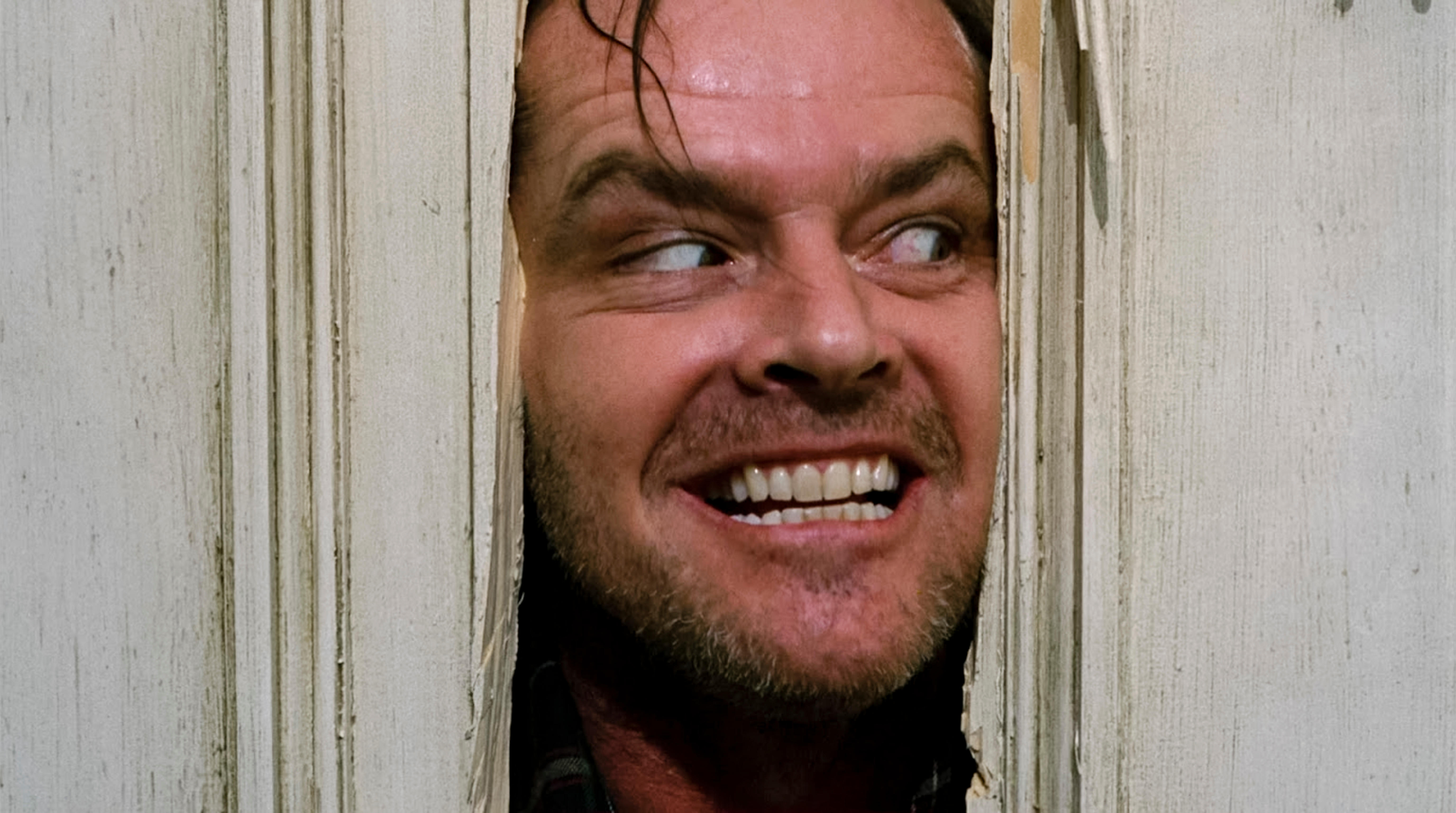 Jack Torrance joué par Jack Nicholson, passant la tête à travers une porte dans The Shining