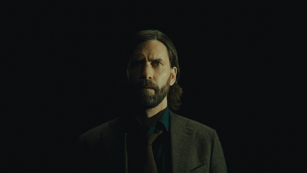 Une image d'Alan Wake dans Alan Wake 2 dans le cadre d'un article sur la façon dont Remedy devrait continuer à utiliser le style Control pour les futurs jeux.  Alan Wake se tient sur un fond sombre, vêtu d'un costume et de cheveux longs et coiffés. 