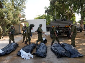 Des soldats israéliens se tiennent à côté des corps d'Israéliens tués par des combattants du Hamas dans le kibboutz de Kfar Azza, dans le sud d'Israël, à environ cinq kilomètres à l'est de Gaza, le 10 octobre 2023.