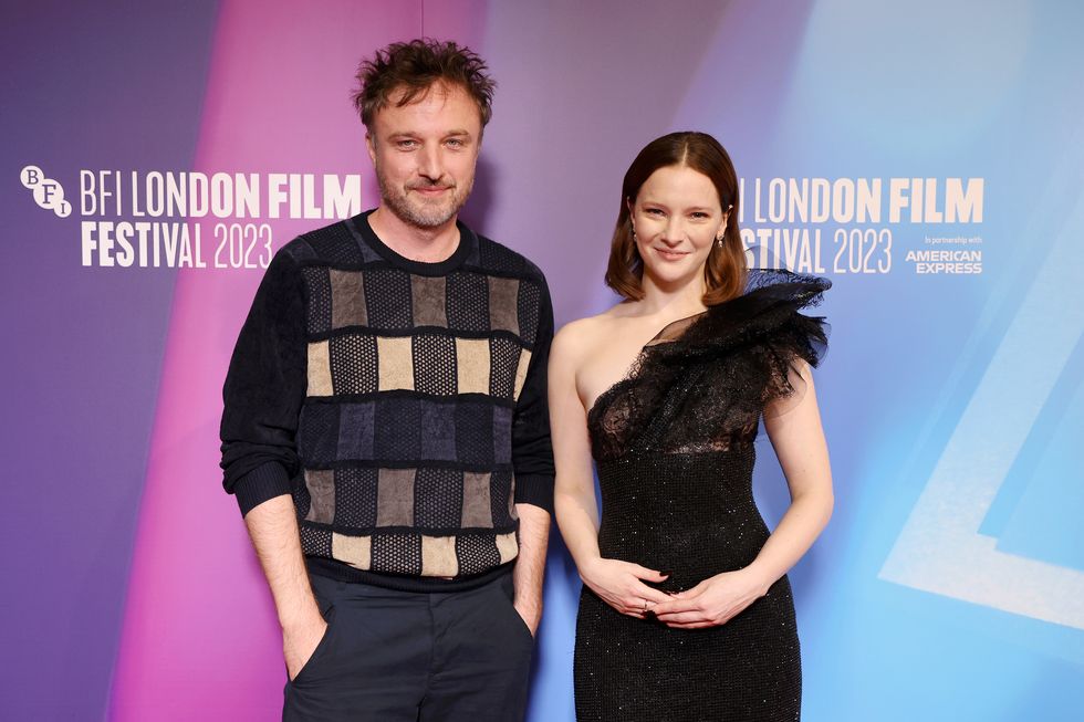 Robert Kokotajlo se tient à côté de Morfydd Clark au festival du film de Londres, il porte un pull noir avec des carrés de différentes couleurs sur le devant, elle porte une robe noire asymétrique ornée de cristaux