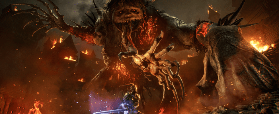 The Spurned Progeny from Lords of the Fallen looms horrifically over a player amidst burning rubble, a clawed hand tearing from its maw to snatch them up.