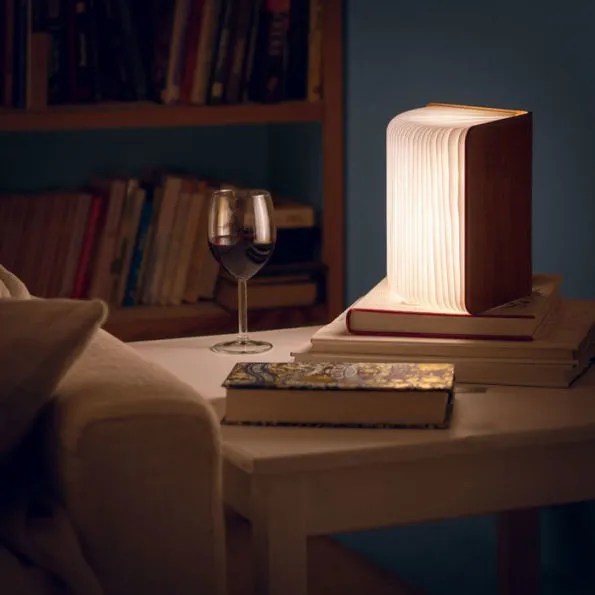 Une lampe de lecture en bois était ouverte sur un bureau à côté d'un livre et d'un verre de vin.