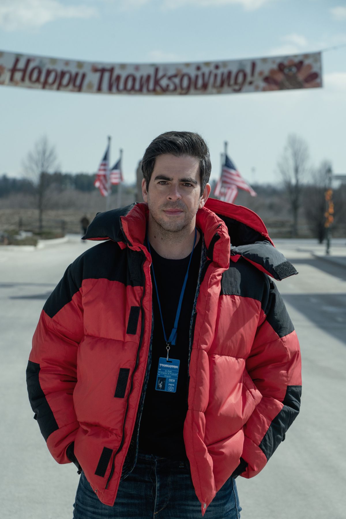 Eli Roth dans une doudoune rouge sur le tournage de Thanksgiving avec une bannière Happy Thanksgiving derrière lui