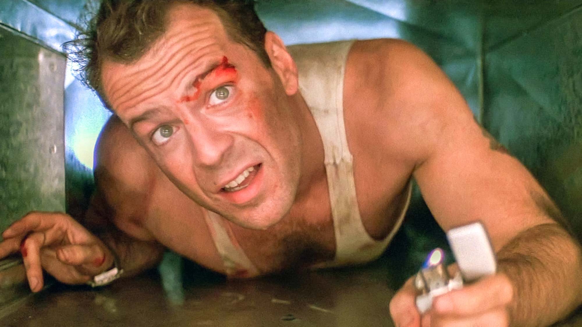 Bruce Willis (dans le rôle de John McClane) rampe dans un évent dans Die Hard, qui est sans doute un film de Noël