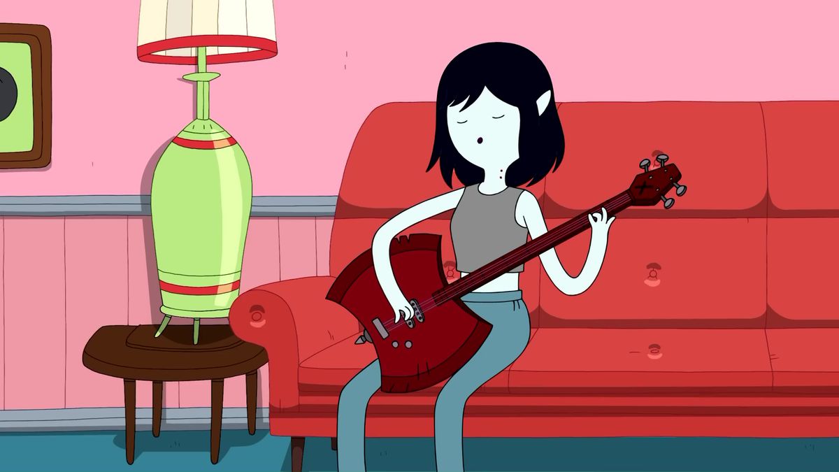 Une image de Marceline la reine vampire assise sur un canapé rouge et jouant de la guitare.  Elle a les cheveux noirs coupés courts et la peau pâle.