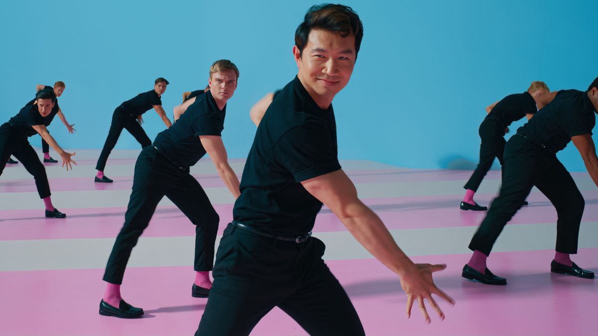 Simu Liu dances with a smirk on his face among a group of fellow Kens in Barbie.