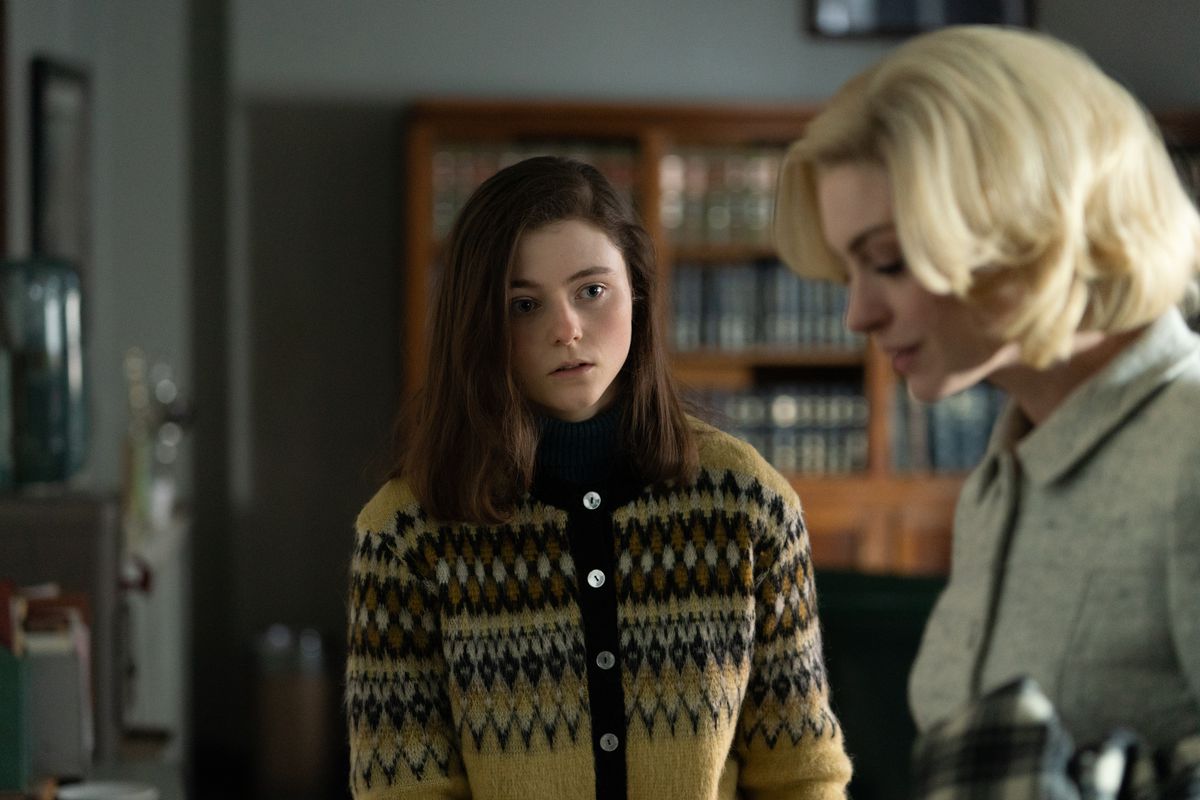 Thomasin McKenzie se tient dans une sorte de pull marron laid et regarde nerveusement une blonde Anne Hathaway faire son travail de bureau, avec glamour, dans le film Eileen.