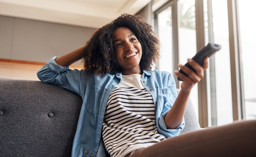 photo d'une jeune femme tenant une télécommande alors qu'elle était assise sur le canapé à la maison