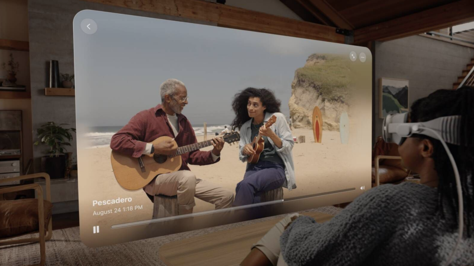 Une dame portant un casque Vision Reality Pro regardant depuis son canapé le souvenir d'un gars jouant de la guitare. 