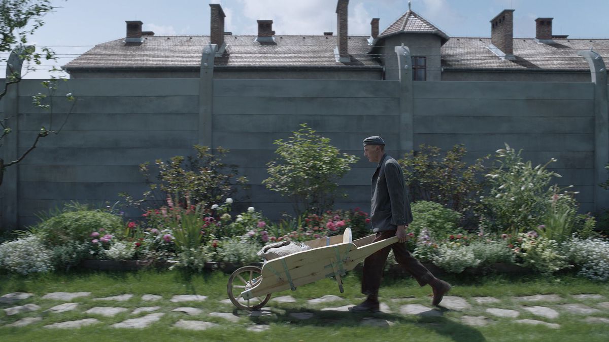 Un jardinier pousse une brouette le long d'un mur de jardin près d'Auschwitz dans la zone d'intérêt 