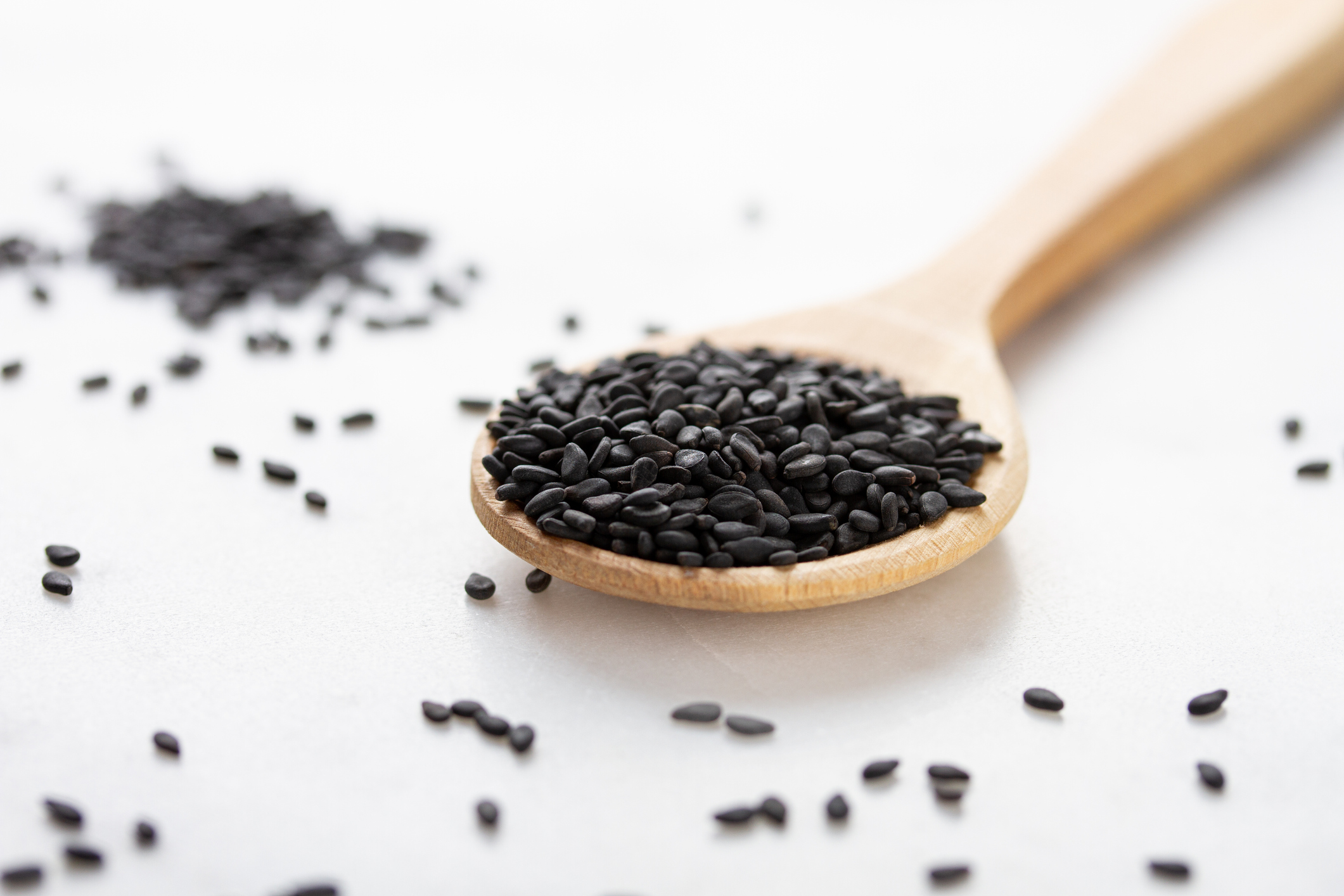 Graines de sésame noires dans une cuillère en bois sur fond blanc