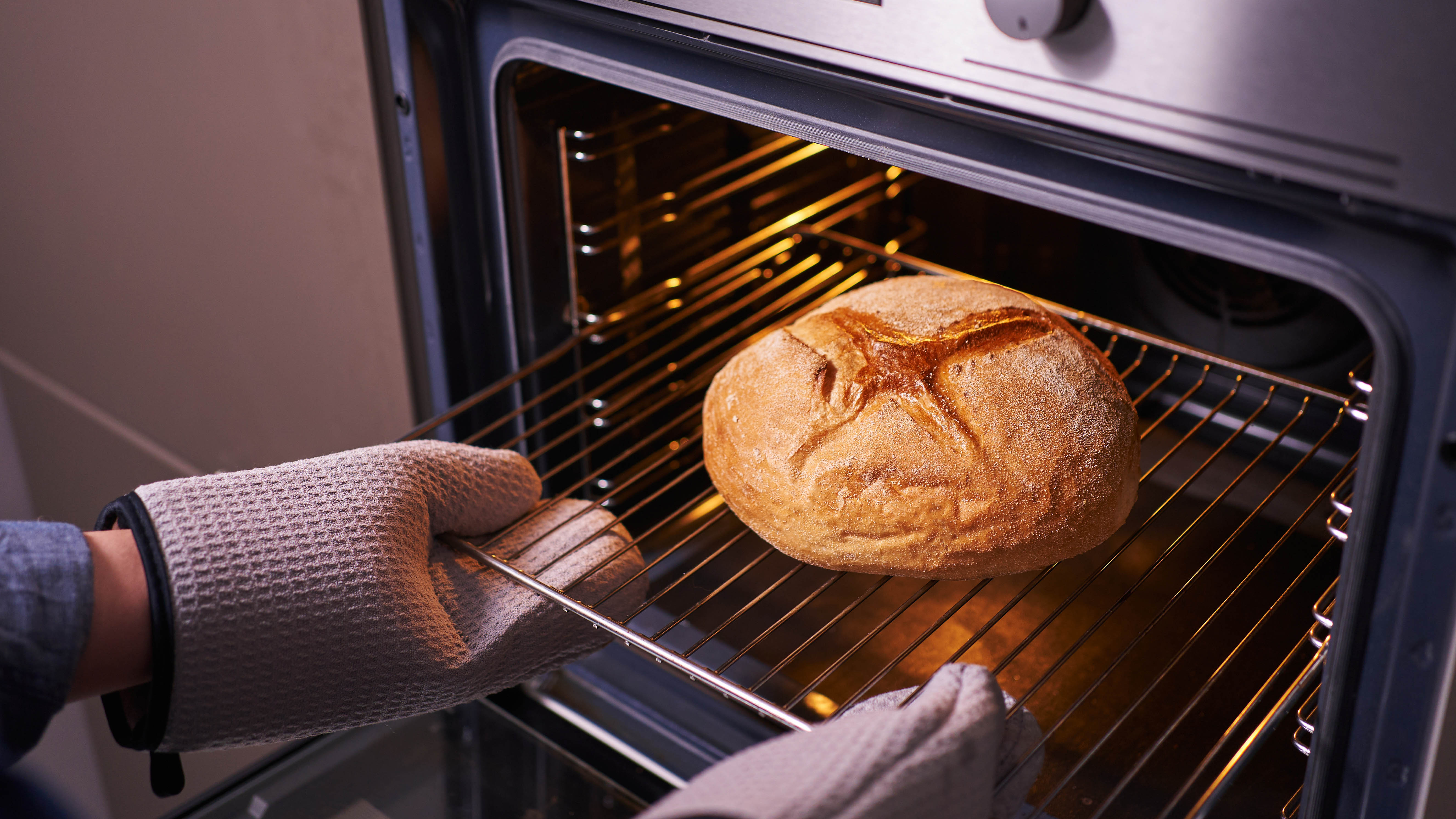 Quelqu'un retire une miche de pain du four tout en portant des gants de cuisine