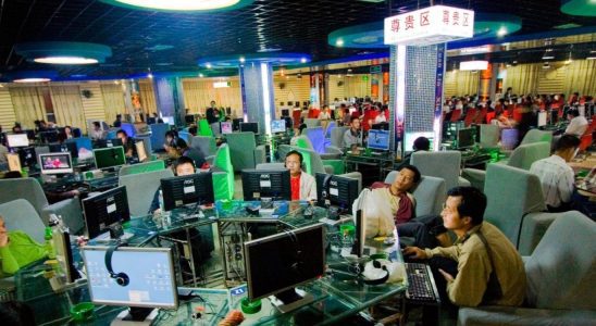 Men sit around a desk in a crowded gaming cafe.