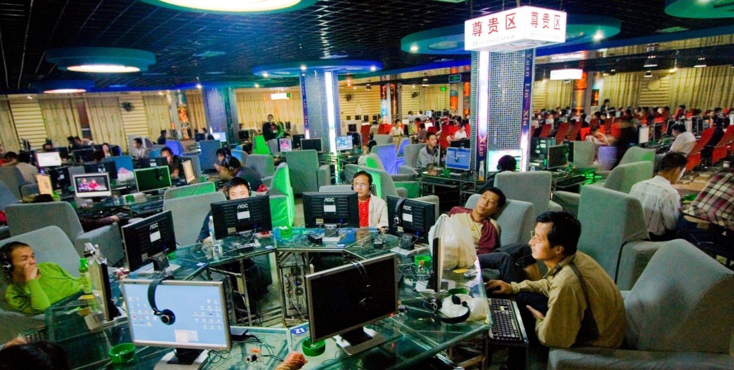 Men sit around a desk in a crowded gaming cafe.