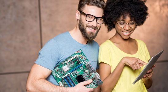 Multi ethnic programmers dressed casually standing together with computer motherboard and digital tablet on the wall background indoors