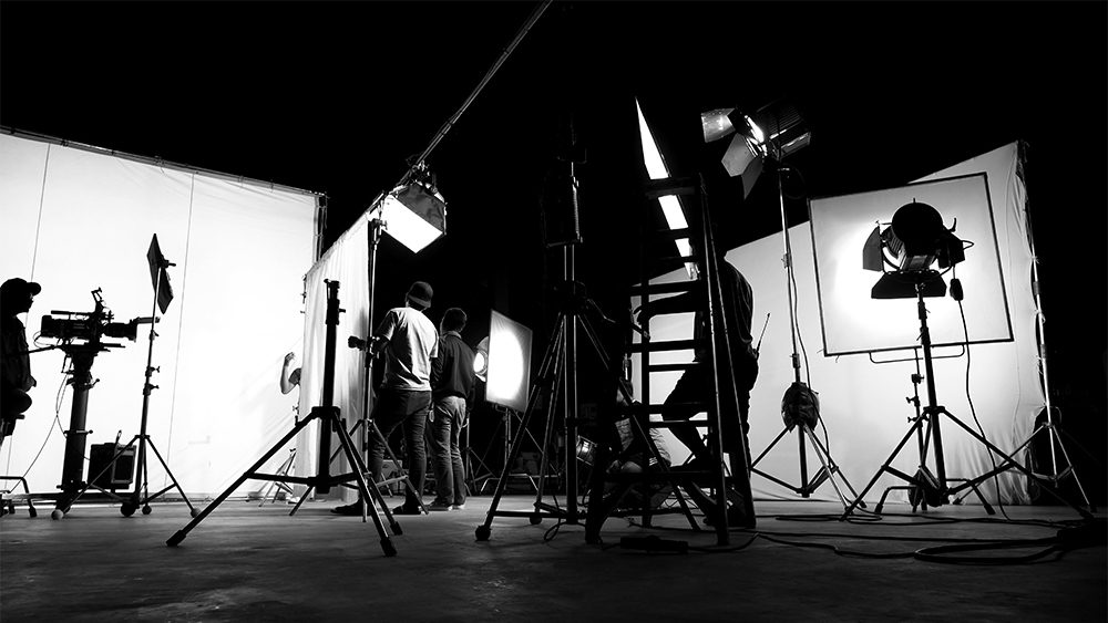 Behind the scenes of TV commercial movie film or video shooting production which crew team and camera man setting up green screen for chroma key technique in big studio.