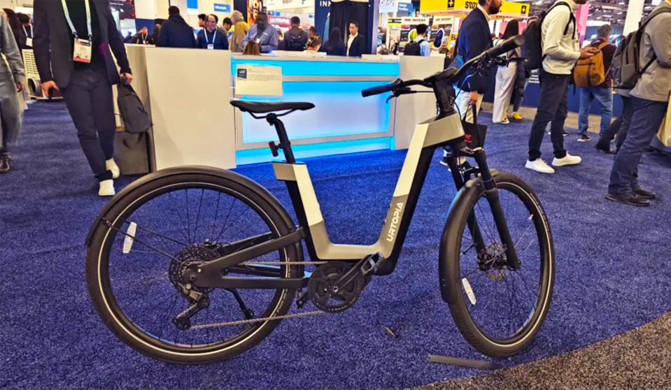 Un vélo électrique Urtopia Fusion gris, blanc et noir repose sur sa béquille sur le tapis bleu du salon CES 2024.