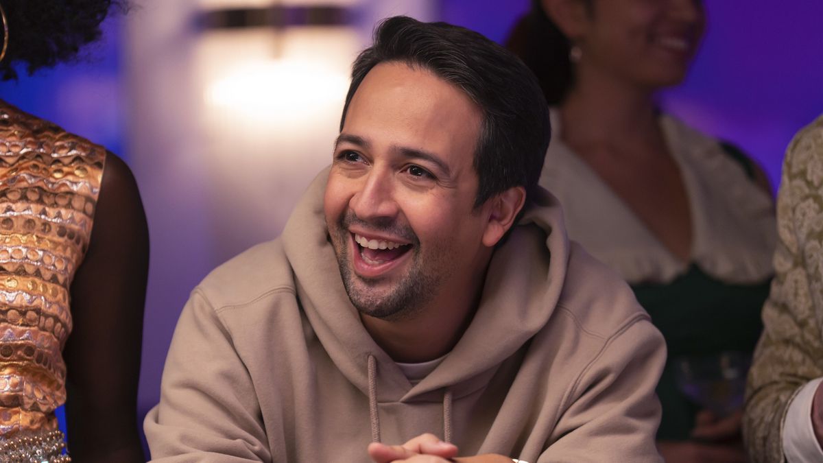 Lin-Manuel Miranda dans le rôle d'Hermès, penché sur une table de poker avec un grand sourire maladroit