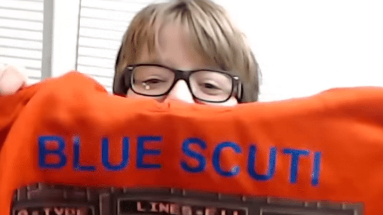 Blue Scuti holds up an orange hoodie with the words 