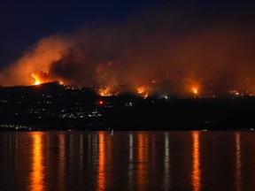 L'incendie de forêt de McDougall Creek brûle à flanc de montagne au-dessus des maisons au bord du lac à West Kelowna, en Colombie-Britannique, le vendredi 18 août 2023.