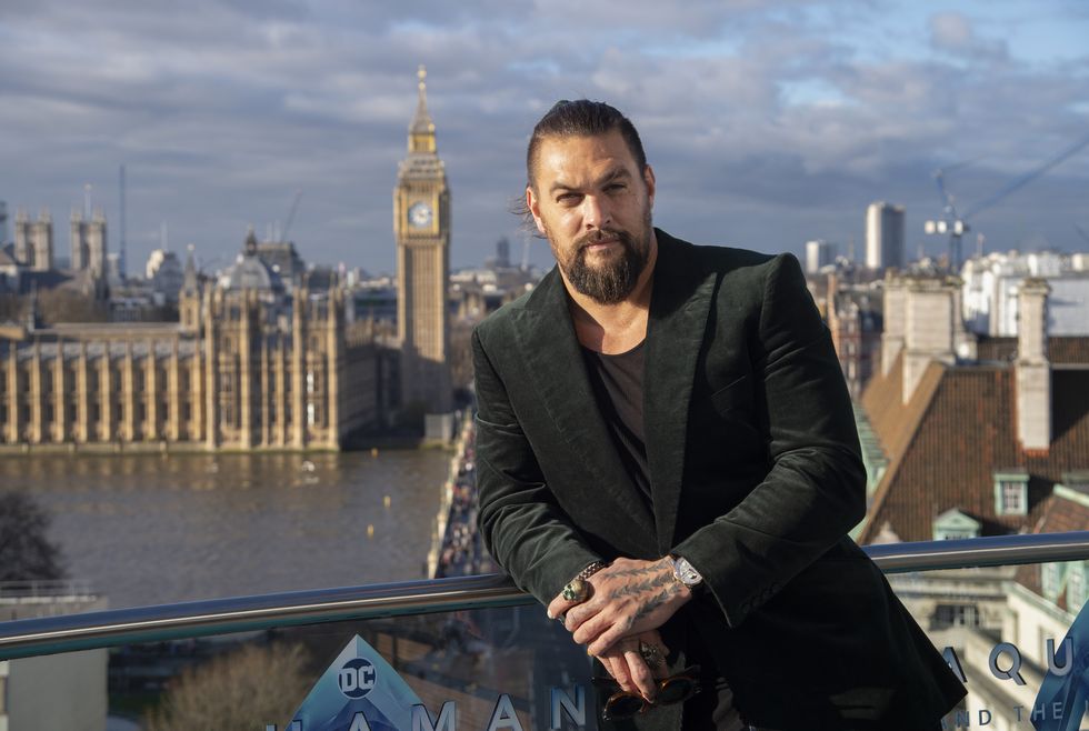 Jason Momoa se tient sur un balcon avec les chambres du Parlement britannique et le centre de Londres en arrière-plan derrière lui