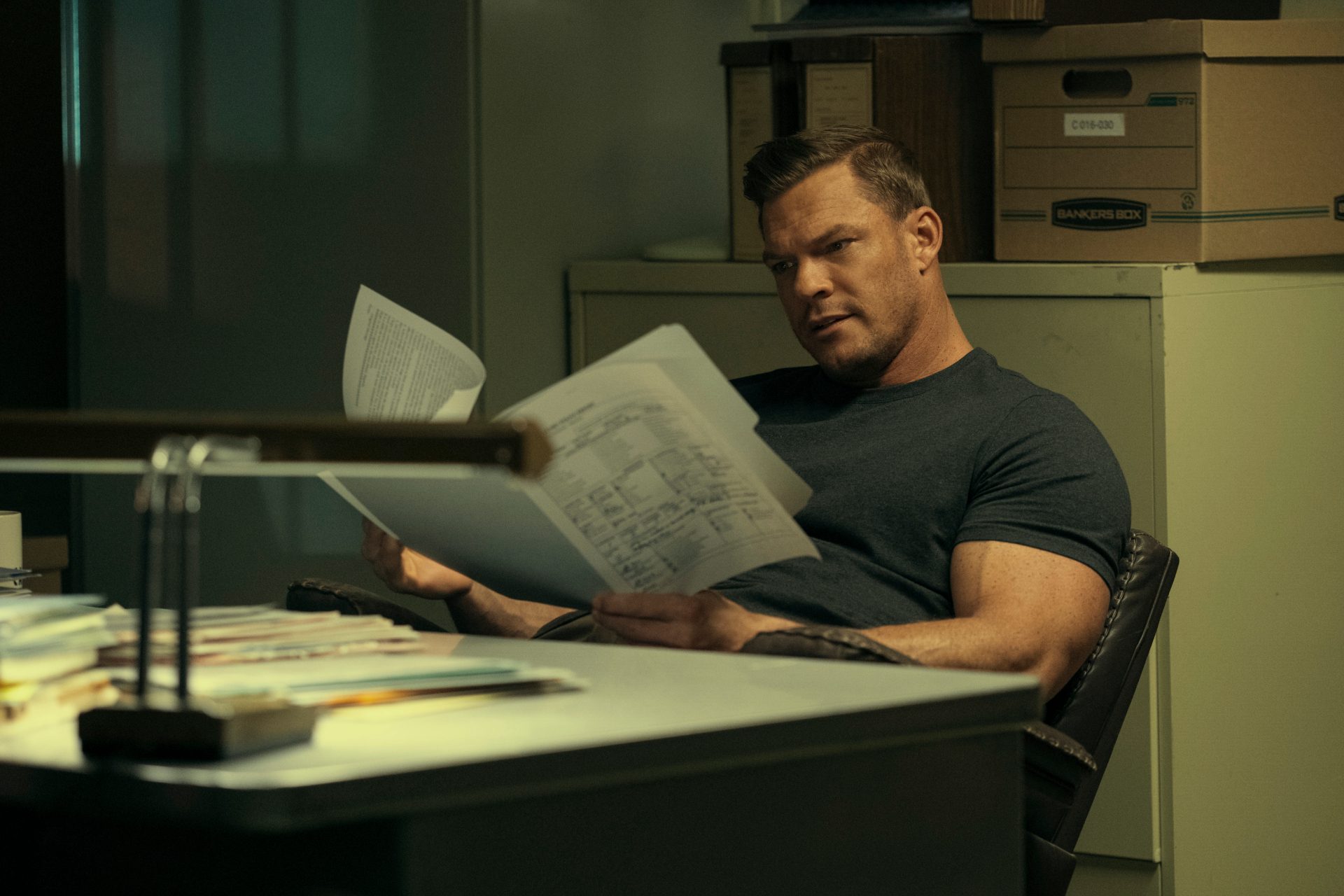 Jack Reacher (Alan Ritchson) sits at a desk combing through files in Prime Video's Reacher