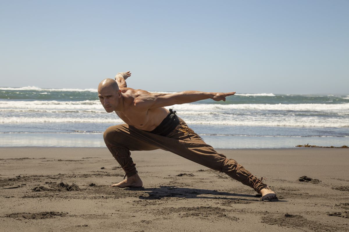 Marko Zaror s'accroupit dans une pose défensive sur une plage de Fist of the Condor, avec l'océan derrière lui.