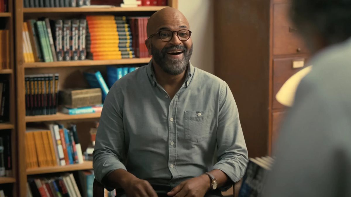 Jeffrey Wright en chemise bleue est assis dans sa bibliothèque en train de rire dans le film American Fiction