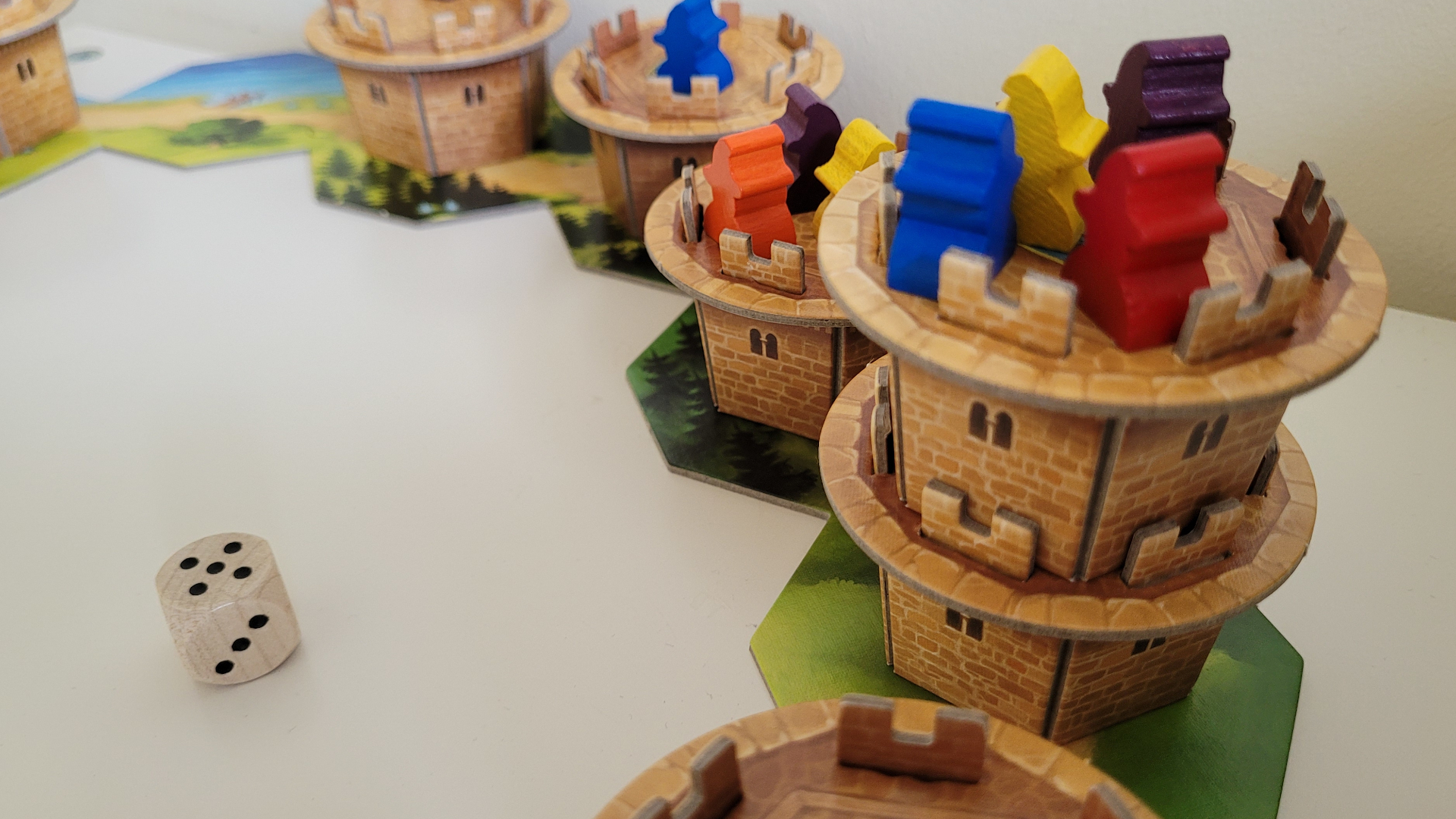 Un demi-cercle de tours en carton provenant de Wandering Towers sur une surface plane, avec des meeples et un dé également en vue