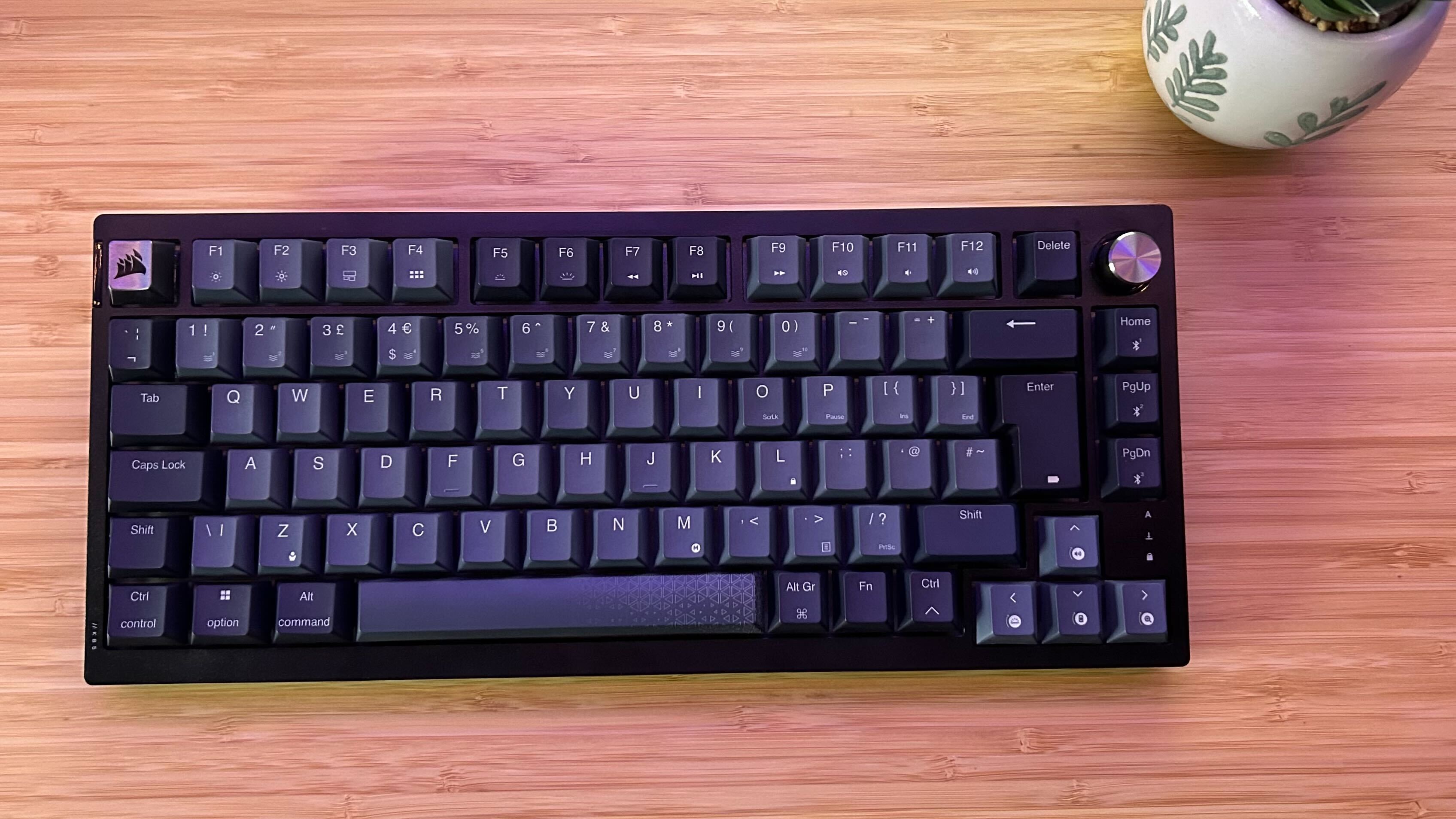 Clavier sans fil Corsair K65 Plus sans RVB sur un bureau en bois avec un pot de plante