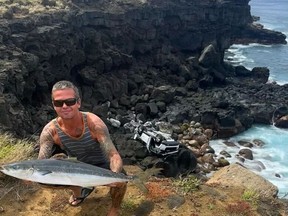 Mike Moody, comme le montre cette image, pêchait au large de la grande île d'Hawaï tôt dimanche lorsqu'un touriste canadien a conduit sa Jeep de location d'une falaise.  Moody pose avec sa prise du jour et la Jeep mutilée du Canadien en arrière-plan sur cette photo non datée