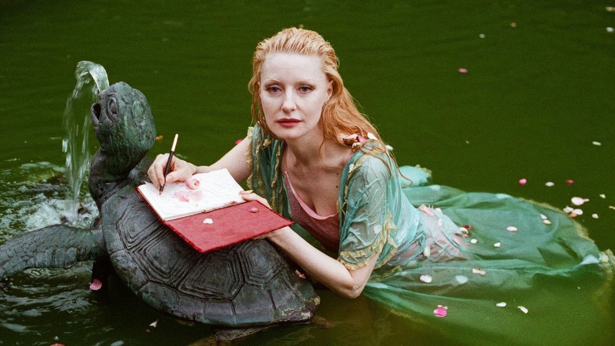 Shere Hite, vêtue d'une robe vert clair, flotte dans l'eau avec un carnet ouvert sur une statue de tortue.  Elle ressemble plus qu'un peu à une sirène.  L'image est tirée du documentaire La Disparition de Shere Hite