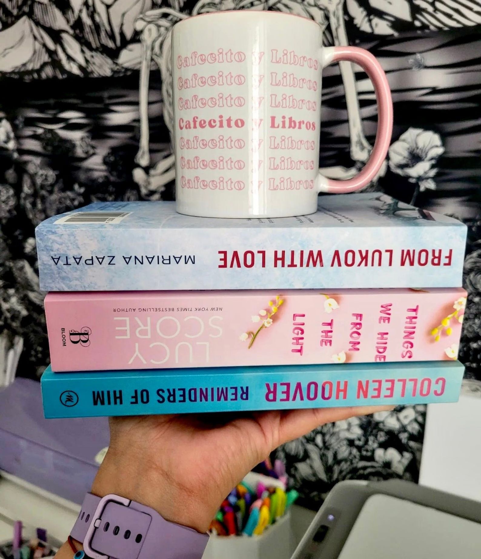 une tasse rose et blanche au-dessus d’une pile de trois livres.  Le texte rose sur la tasse dit : "cafécito et livres"