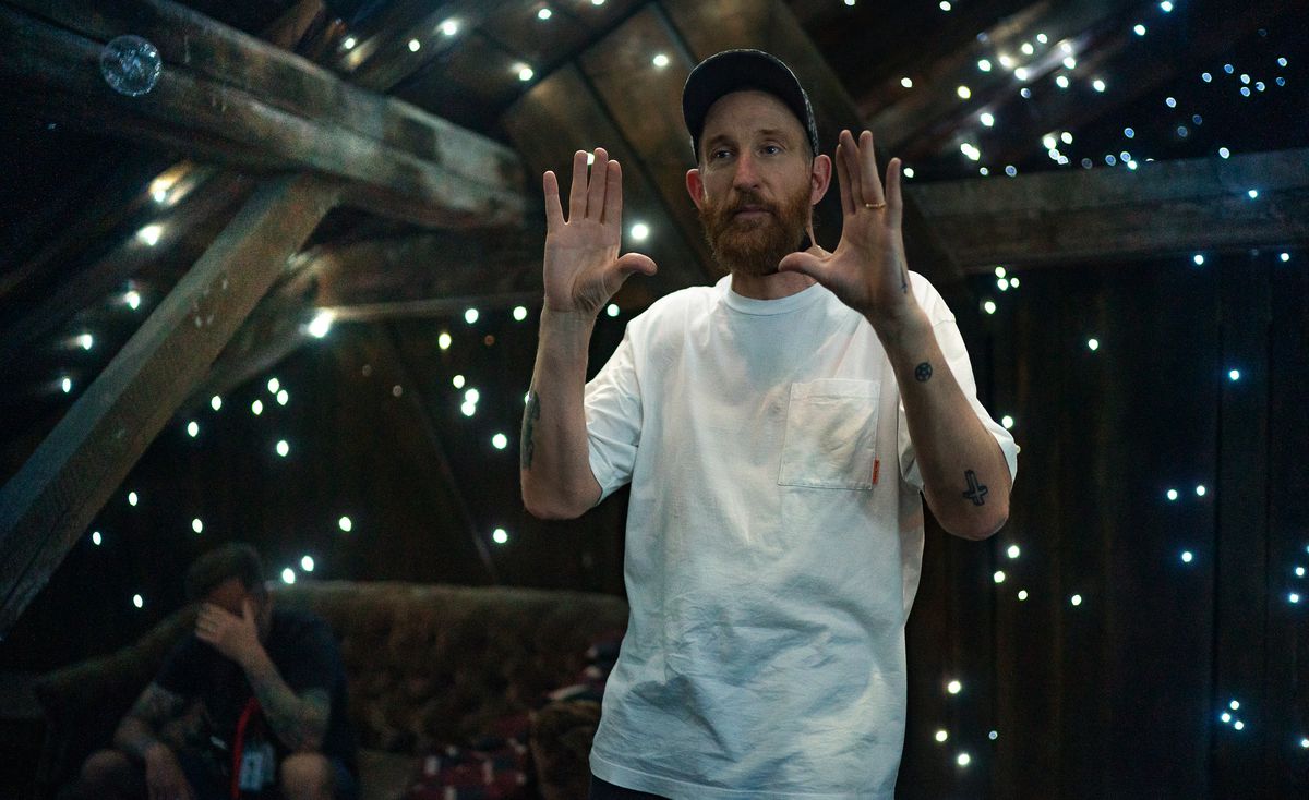 Le réalisateur Johan Renck, vêtu d'un T-shirt blanc, se tient sur le plateau de son film Spaceman, dans un espace noir entouré de poutres en bois nues et de points de lumière en forme d'étoiles.