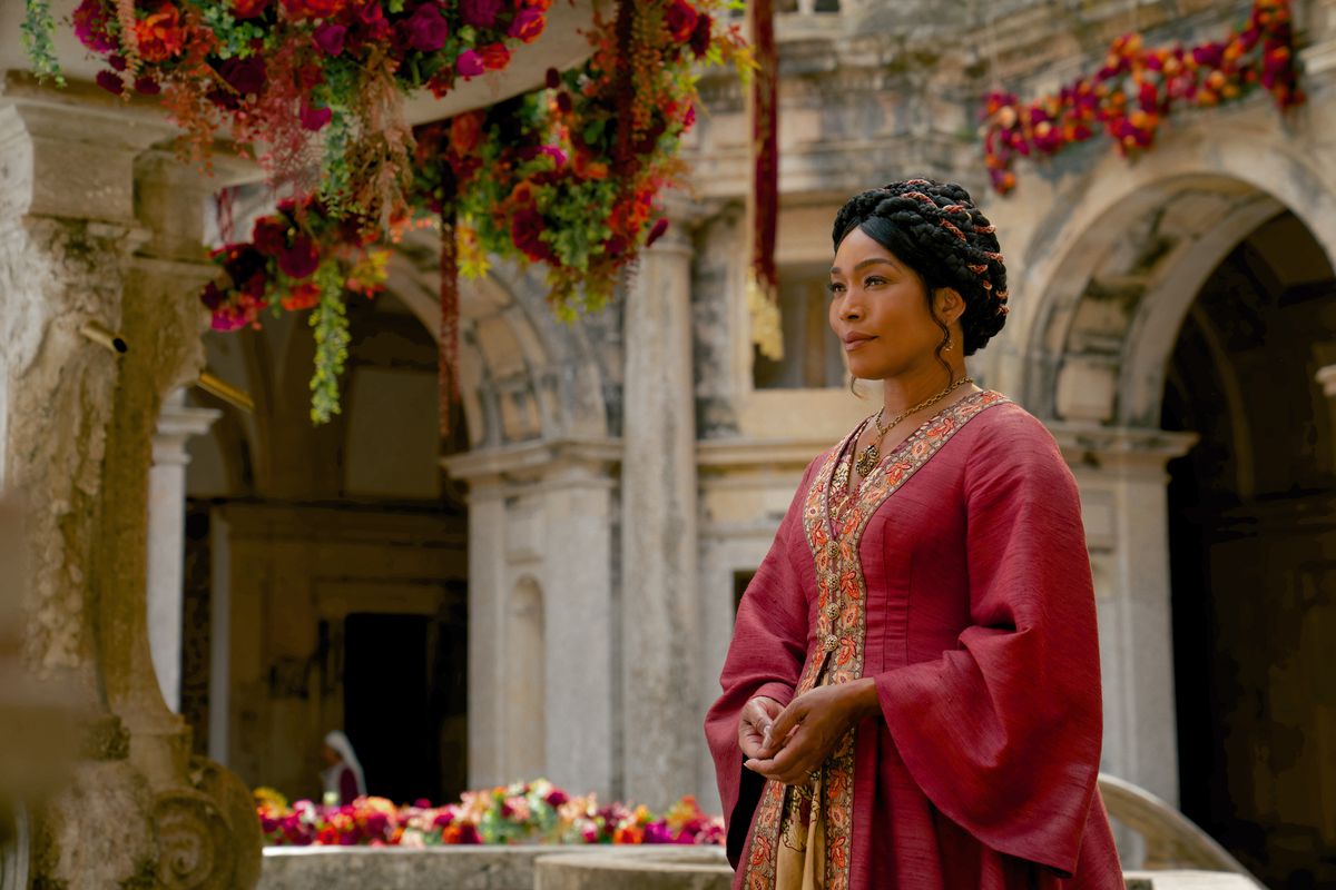 Angela Bassett dans une robe rouge royale de style fantastique médiéval, debout dans une cour-jardin