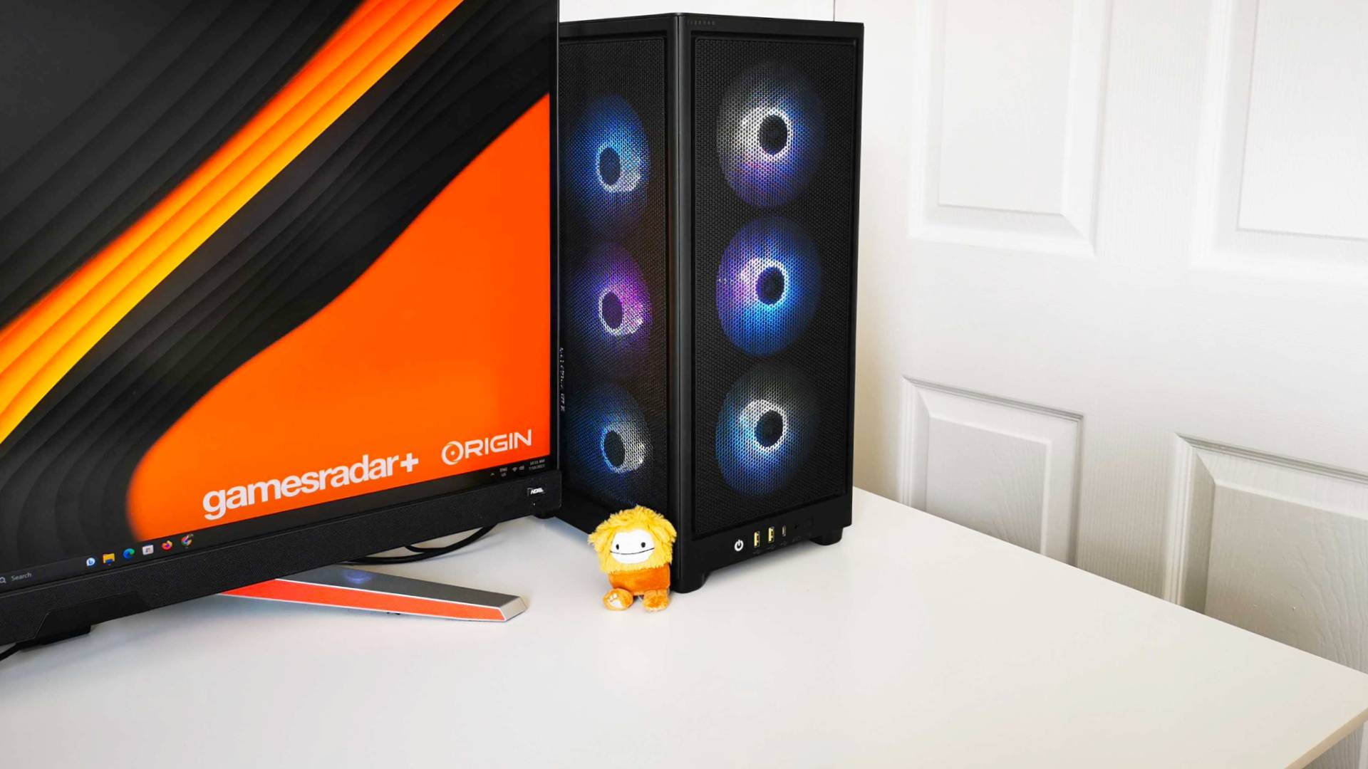 PC de jeu Origin Chronos V3 sur un bureau blanc à côté du moniteur