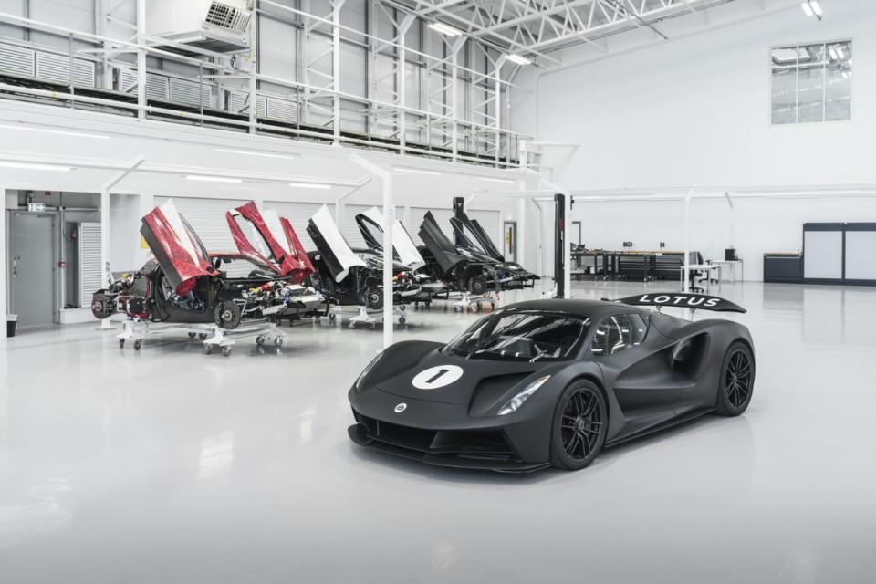 Image du hall de production Lotus Evija avec une série de modèles à moitié terminés en arrière-plan, tandis qu'au premier plan se trouve une Evija noire en livrée de course.