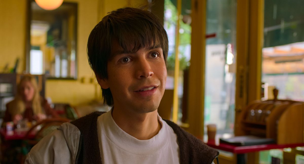 Julio Torres souriant dans un sweat à capuche dans un restaurant de New York dans le film Problemista