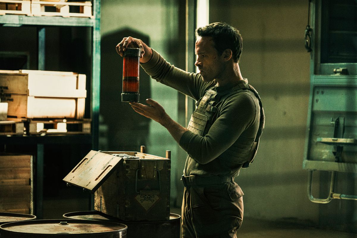 Un homme vêtu d'un gilet en kevlar tenant un grand récipient de nitroglycérine dans The Wages of Fear (2024).