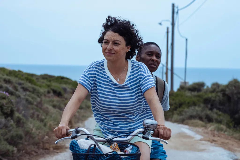 Une femme qui monte à l’arrière d’un vélo tandis qu’une autre femme pédale et sourit.