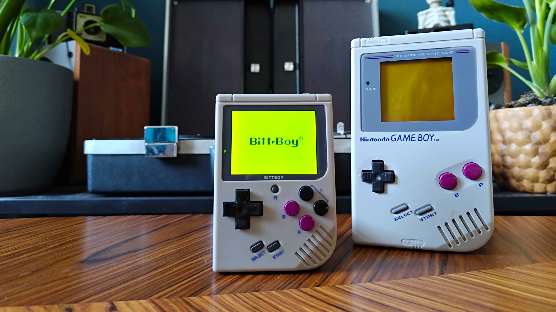 Ordinateur de poche Bittboy à côté d'un Game Boy sur une table en similibois