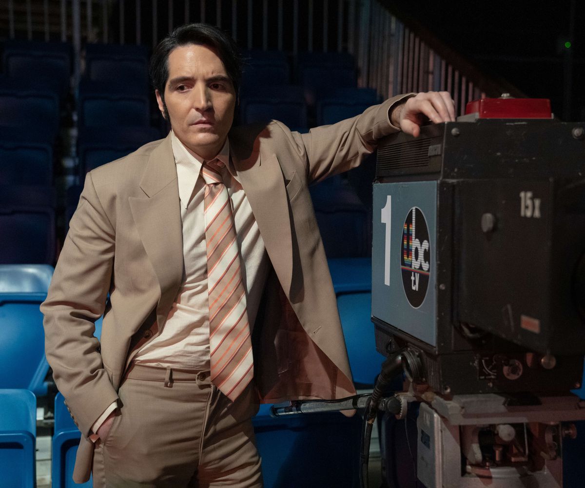 David Dastmalchian dans le rôle de Jack Delroy dans Late Night with the Devil vêtu d'un costume et appuyé contre une caméra