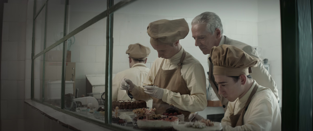 Un chef regardant par-dessus l'épaule de deux personnes préparant des pâtisseries dans The Platform