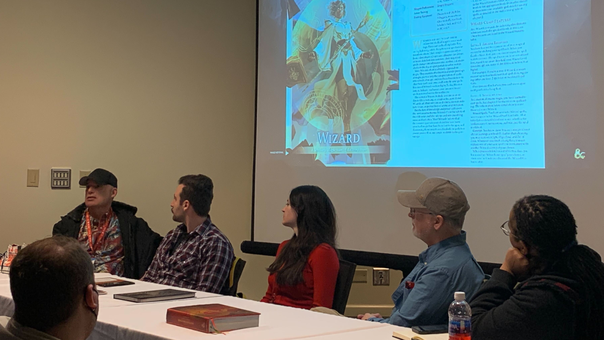 Chris Perkins et le panel D&D discutent du nouveau manuel du joueur à Garycon, avec des images sur un projecteur derrière eux.