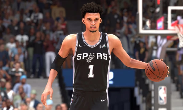 Capture d'écran promotionnelle de NBA 2K24, montrant la recrue des Spurs, Victor Wembanyama, dribblant le ballon sur le terrain.  Stade plein de supporters visibles derrière lui.