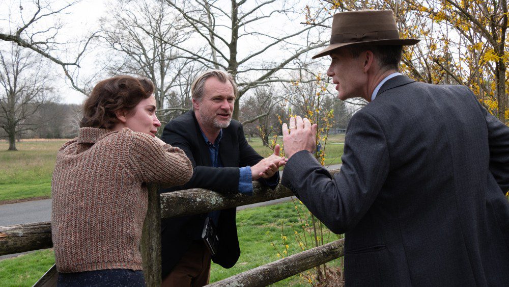 L to R: Emily Blunt (as Kitty Oppenheimer) with writer, director, and producer Christopher Nolan and Cillian Murphy (as J. Robert Oppenheimer) on the set of OPPENHEIMER.