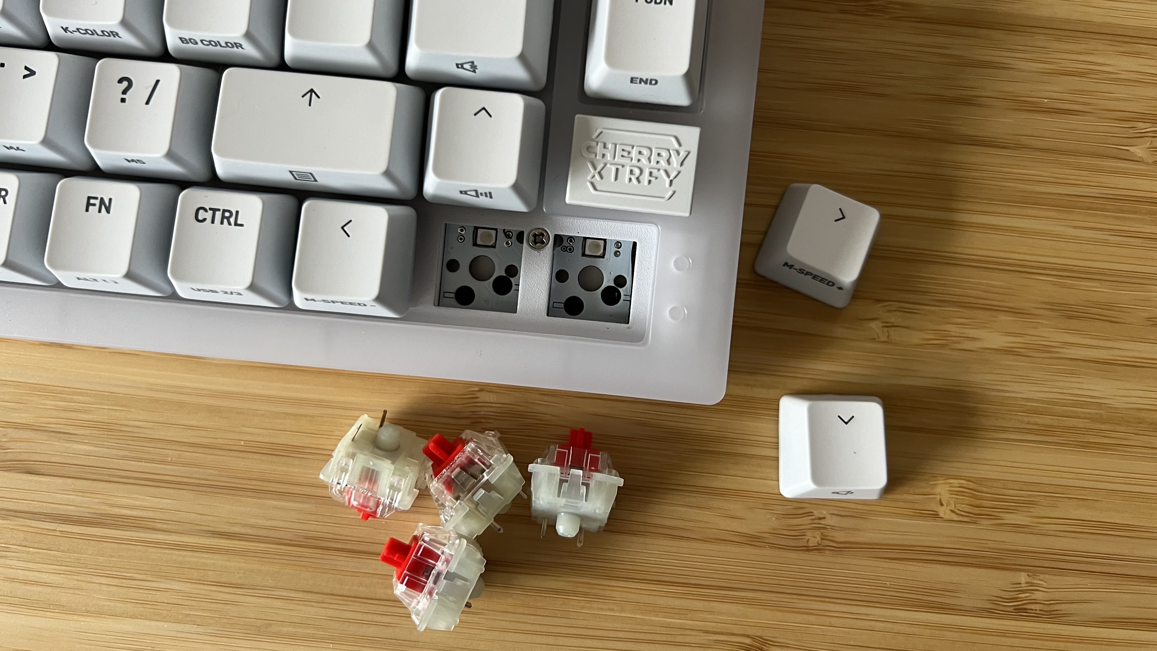 Coin du clavier Cherry XTRFY K5V2 avec commutateurs et touches retirés et placés sur le côté sur une table en bois