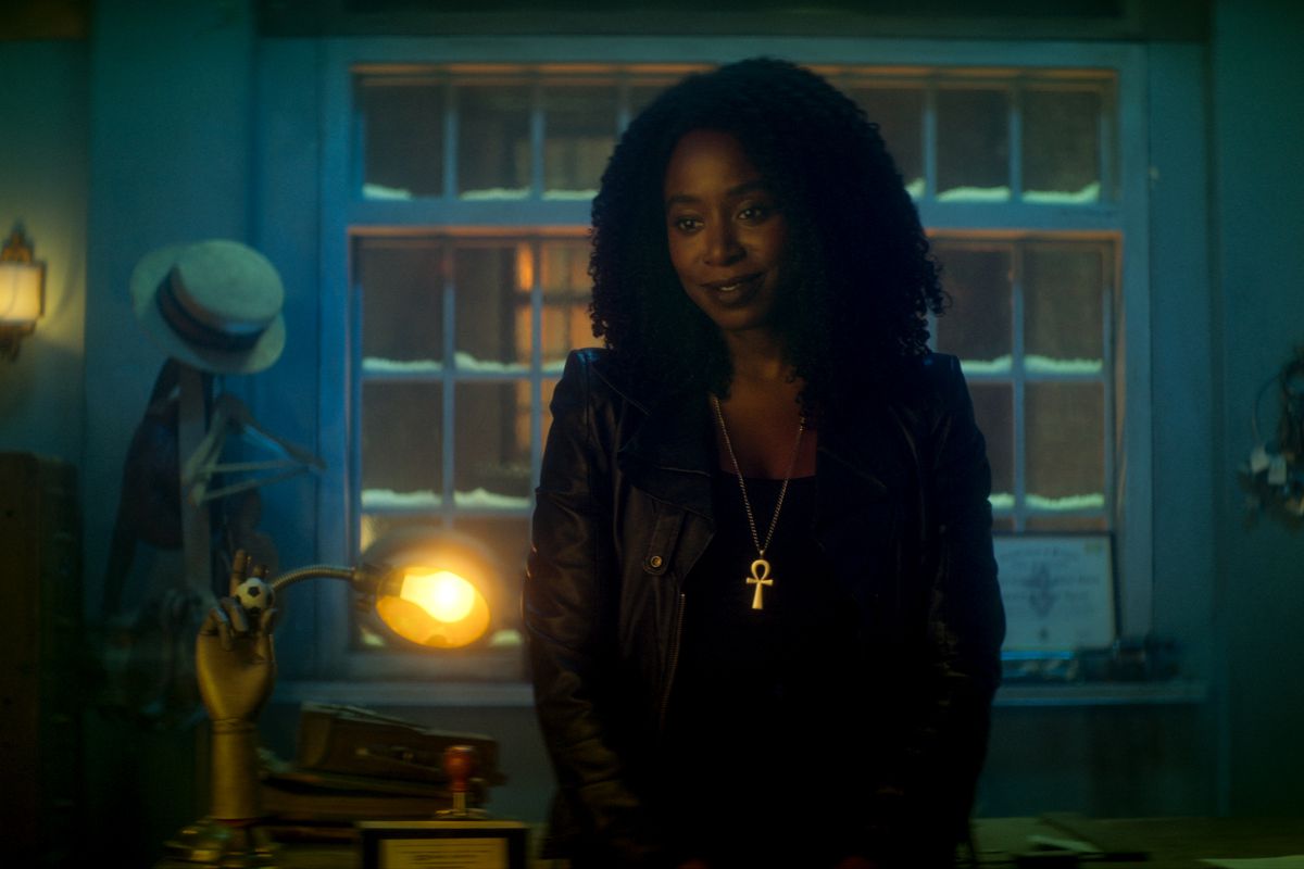 Kirby Howell-Baptiste dans le rôle de la mort dans Dead Boy Detectives.  Elle est vêtue de noir, avec un collier ankh en or, debout dans une pièce teintée de bleu.